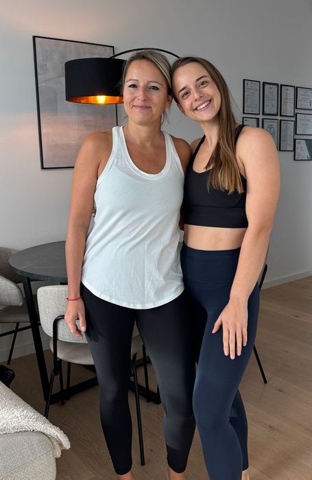 Lili Nowicki in Sportkleidung Arm in Arm mit einer Klientin im Wohnzimmer